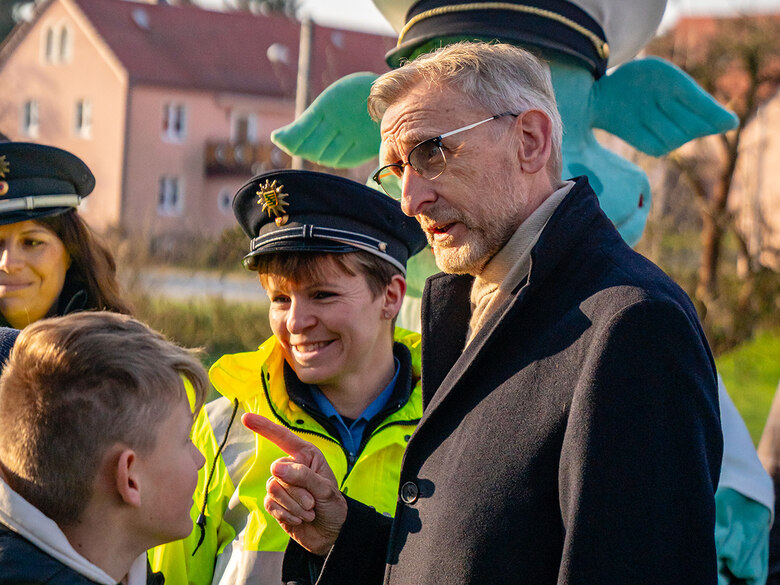 Blitz für Kids: Staatsminister Armin Schuster spricht mit Schulkindern. Im Hintergrund steht eine Polizistin mit gelber Warnweste.