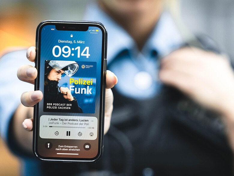 Podcast der Polizei Sachsen: Zu sehen ist der Bildschirm eines Smartphones. Das »PolizeiFunk«-Logo ist zu sehen. Das Handy wird von einer Polizeibeamtin gehalten.