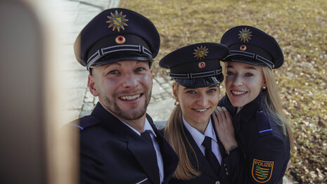 Vor der feierlichen Ernennung nach der Ausbildung bei der Polizei Sachsen in Chemnitz: Ein Polizeimeisteranwärter sowie zwei Anwärterinnen schauen für ein Foto direkt in die Kamera. Die jungen Menschen tragen Polizeiuniform.