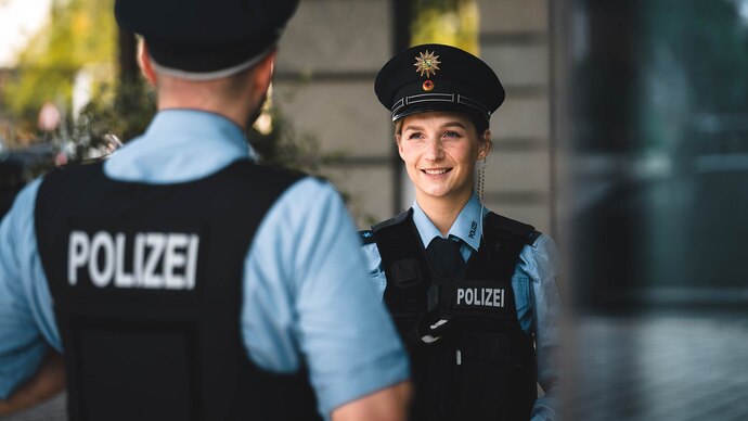 So kann es nach Ausbildung oder Studium bei der Polizei weitergehen: Eine Streifenpolizistin in blauer Uniform unterhält sich mit einem Kollegen. Auf ihrer Mütze ist das Wappen des Freistaats Sachsen zu sehen.