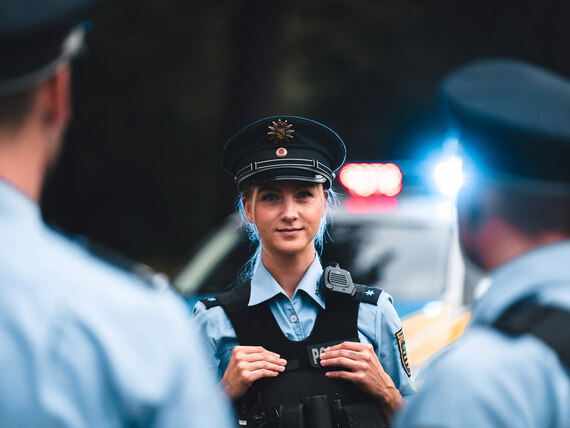 Ausbildung oder Studium? Mit beidem gibt’s sichere Berufsperspektiven! Eine junge Polizistin in Polizeiuniform vor einem Streifenwagen.