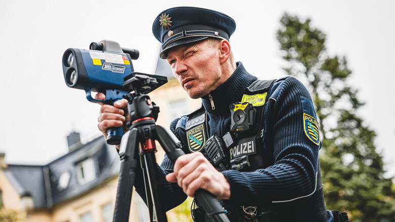 Ein Polizist der Polizei Sachsen in Uniform bei einer Geschwindigkeitsmessung – Verkehrskontrollen wie diese tragen zur Sicherheit im Straßenverkehr bei.