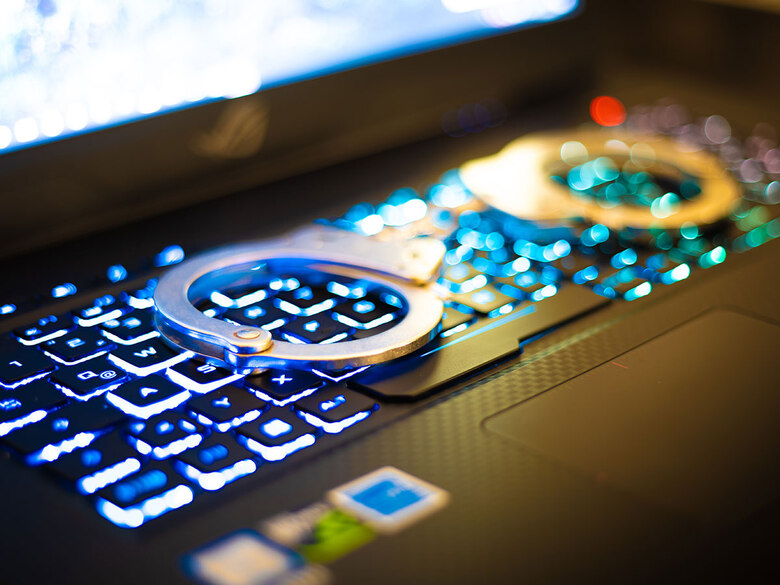 Nachwuchswerbung Cybercrime: Silberne Handschellen liegen auf einem aufgeklappten Laptop. Die Tastatur leuchtet blau.