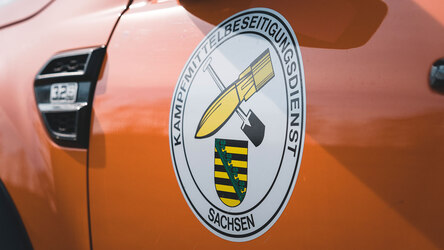 Auf einem orangenen Einsatzfahrzeug des Polizeiverwaltungsamtes ist das Logo des Kampfmittelbeseitigungsdienstes (KMBD) zu sehen.