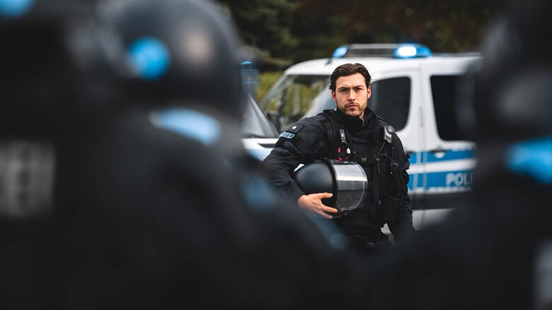 Nur eine der vielfältigen Berufsperspektiven nach Ausbildung oder Studium bei der Polizei Sachsen: Ein Einsatzbeamter der Bereitschaftspolizei in Uniform und mit Helm vor einem Streifenwagen.