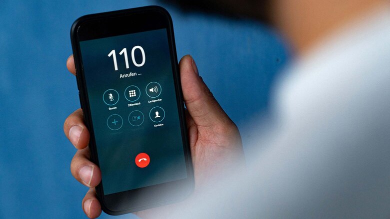 Auf einem Smartphone ist die Notruf-Nummer 110 der Polizei zu sehen. Das Handy wählt gerade die Telefonnummer, im Hintergrund ist eine blaue Wand.