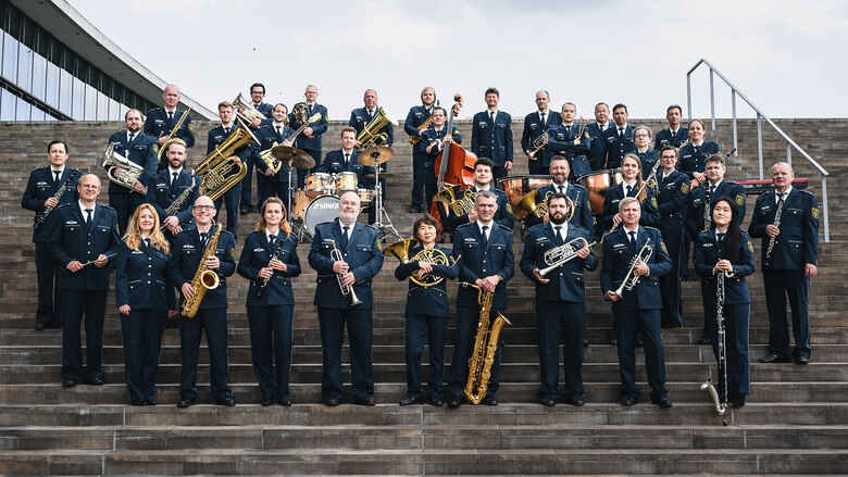 Die Musikerinnen und Musiker des Polizeiorchesters der Polizei Sachsen haben sich zu einem Gruppenfoto versammelt. Sie tragen ihre Uniformen und halten ihre Instrumente in der Hand.