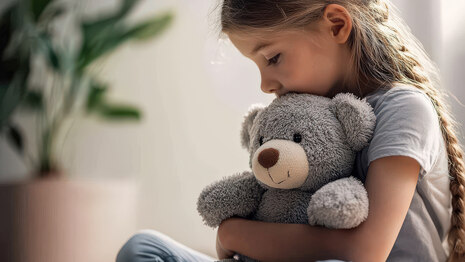 Trauriges Mädchen sitzt auf Boden und klammert sich an Teddybär